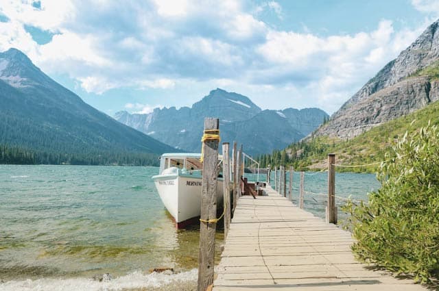 A scenic mountainous landscape behind a turquoise lake. A rowing boat is waiting 